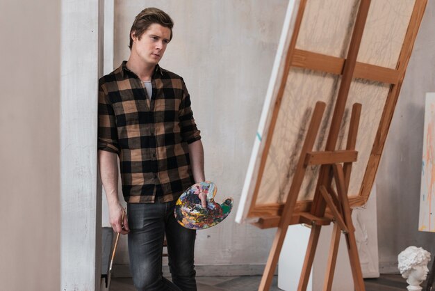 Молодой художник смотрит на свою картину в студии
