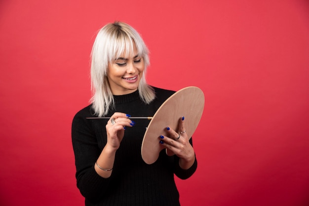 Young artist woman holding art supplies on a red wall. 