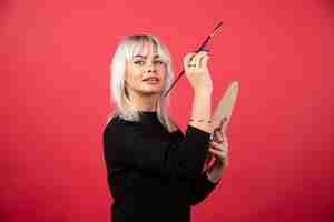 Free photo young artist woman holding art supplies on a red wall.