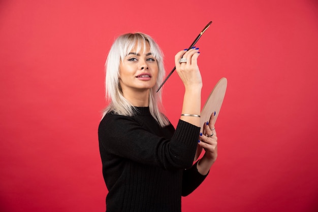 Young artist woman holding art supplies on a red wall. 