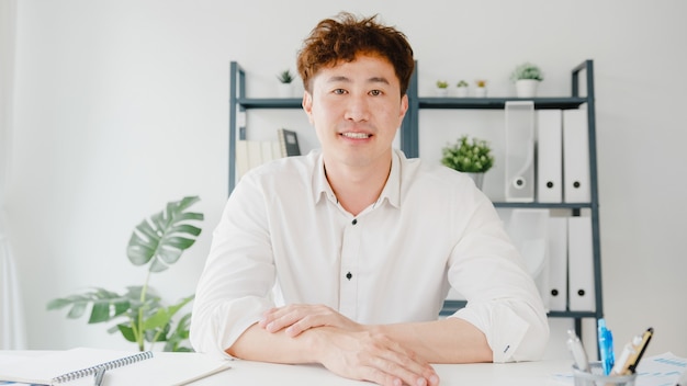 Young Asia businessman using computer laptop talk to colleagues about plan in video call meeting while working from home at living room.