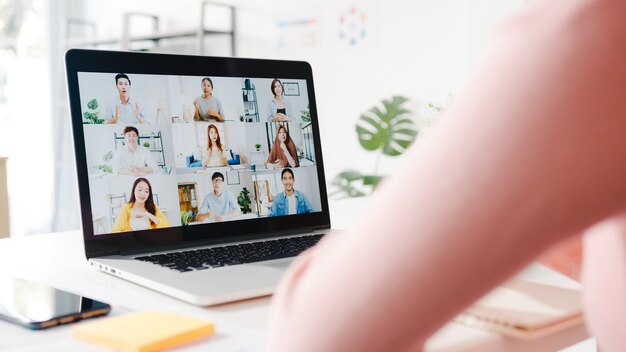 Young Asia businesswoman using laptop talk to colleague about plan in video call meeting while work from home at living room.