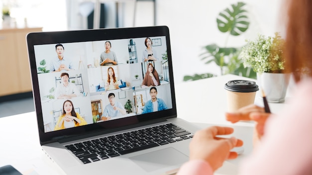 Young Asia businesswoman using laptop talk to colleague about plan in video call meeting while work from home at living room.