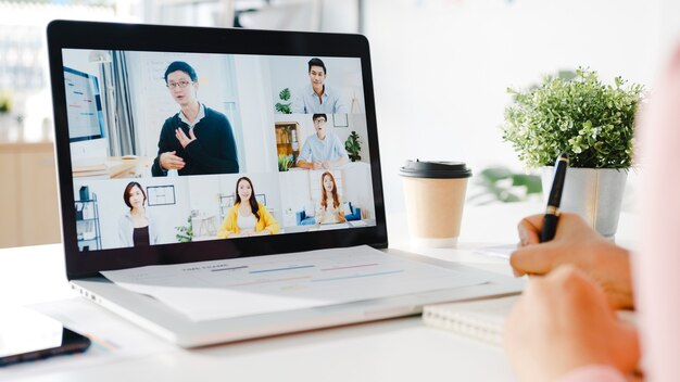 Young Asia businesswoman using laptop talk to colleague about plan in video call meeting while work from home at living room.