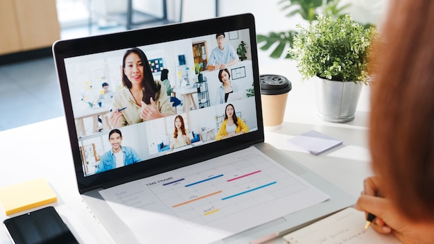 Young Asia businesswoman using laptop talk to colleague about plan in video call meeting while work from home at living room.