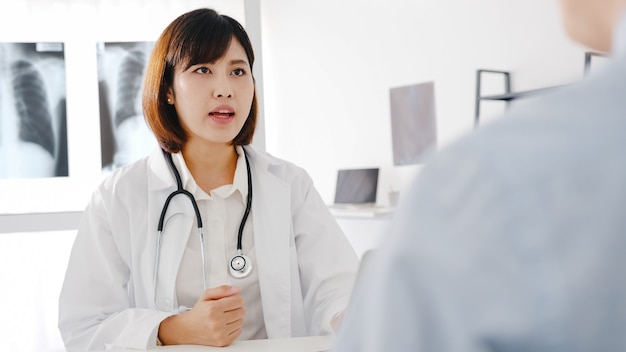 컴퓨터 노트북을 사용하는 흰색 의료 제복을 입은 젊은 아시아 여성 의사가 좋은 소식을 전달하고 있습니다.