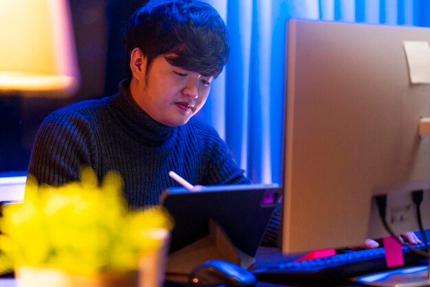 Молодой азиатский внештатный креативный дизайнер-программист фокусирует рабочую руку, используя ручку с планшетом, думая, концентрируется, работает допоздна дома сверхурочно ночью при слабом освещении в гостиной с городским боке