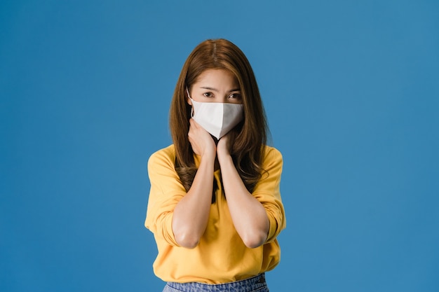 Young Asia girl wear medical face mask, tired of stress and tension, looks confidently at camera isolated on blue background. Self-isolation, social distancing, quarantine for corona virus prevention.