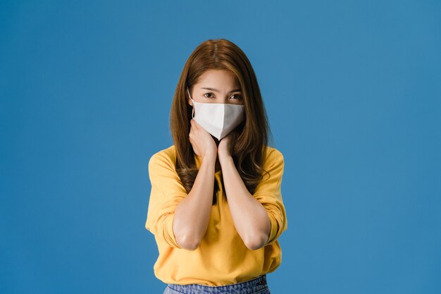 Young Asia girl wear medical face mask, tired of stress and tension, looks confidently at camera isolated on blue background. Self-isolation, social distancing, quarantine for corona virus prevention.