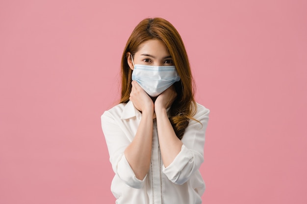 젊은 아시아 소녀는 스트레스와 긴장에 지친 의료 얼굴 마스크를 착용하고 분홍색 배경에 고립 된 카메라에서 자신있게 보인다.