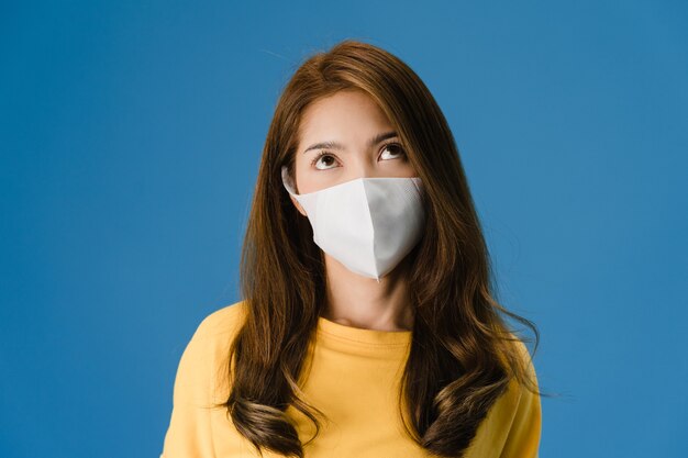 Young Asia girl wear medical face mask, tired of stress and tension, looks confidently at space isolated on blue background. Self-isolation, social distancing, quarantine for corona virus prevention.