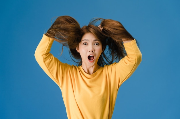 Giovane donna asiatica che sente felicità con l'espressione positiva, funky gioiosa sorpresa, vestita in un panno casual e guardando la telecamera isolata su sfondo blu. la donna felice adorabile felice si rallegra del successo