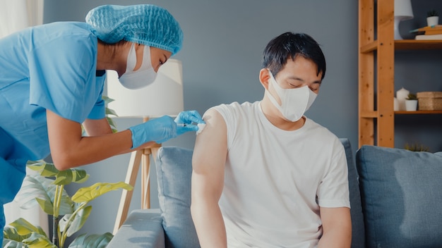 Young Asia lady nurse giving Covid-19 or flu antivirus vaccine shot to male patient wear face mask protection from virus disease