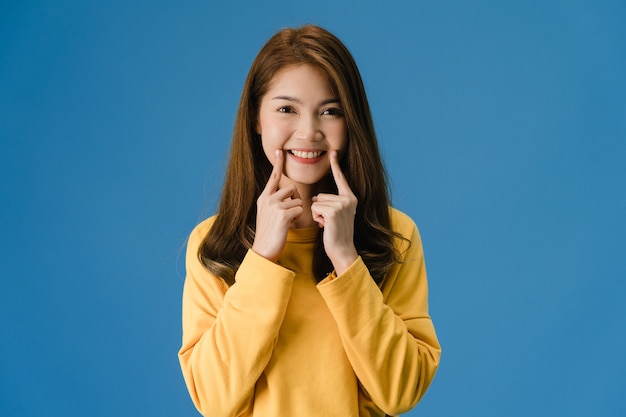 Young Asia lady showing smile, positive expression, dressed in casual cloth and look at camera isolated on blue background. Happy adorable glad woman rejoices success. Facial expression concept.