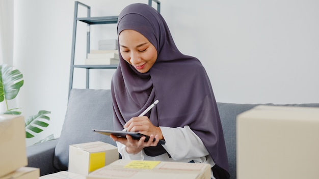 Young asia muslim businesswoman check product purchase order on stock and save to tablet computer work at home office.