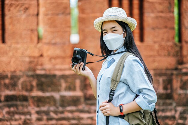 유적지를 여행하는 동안 모자와 보호 마스크를 쓴 젊은 아시아 배낭 여성