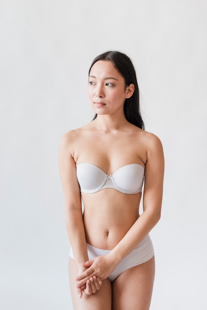 Young Asian brunette in bra and underpants against white background