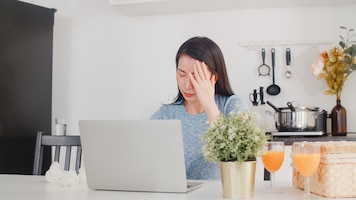 Young asian business woman records of income and expenses at home. lady worried, serious, stress while using laptop record budget, tax, financial document working in modern kitchen at house .