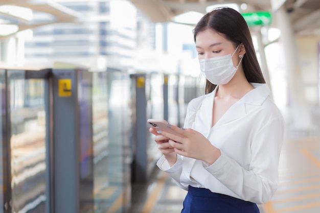長い​髪​の​若い​アジア人​ビジネス​ウーマン​は​、​医療用​フェイス​マスク​を​着用して​、​コロナ​ウイルス​（​covid​-​19​）​から​健康​を​守り​、​h​で​スマート​フォン​を​使用している​ときに​病気​の​ウイルス​や​ほこり​pm​.​2​.​5​または​病原体​を​防ぎます
