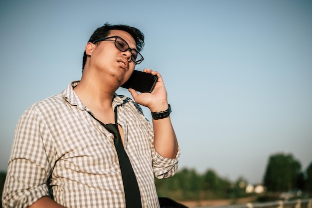 셔츠와 넥타이를 매고 반바지와 안경을 쓴 젊은 아시아 사업가가 야외 복사 공간에서 스마트폰을 사용합니다.