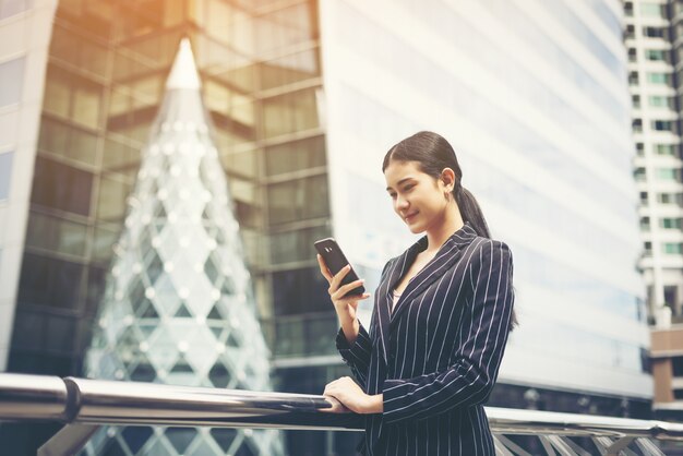 Young asian businesswoman using at mobile smartphone.Young female professional in the city in front of big building.