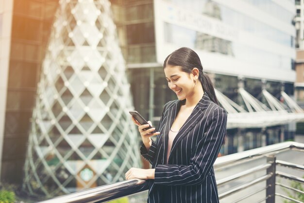 Молодой азиатский бизнесмен, используя на мобильный смартфон. Молодая женщина-профессионал в городе перед большим зданием.