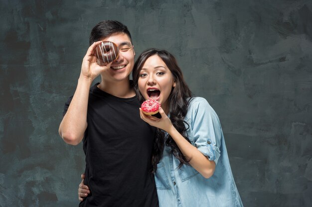 若いアジアのカップルは甘いカラフルなドーナツを食べることを楽しむ