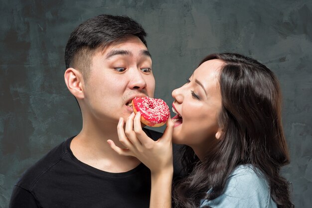 若いアジアのカップルは甘いカラフルなドーナツを食べてお楽しみください