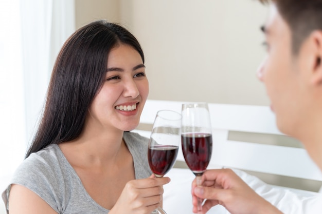 젊은 아시아 부부는 와인을 들고 행복 들고 유리 침실에서 축하