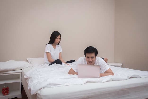 Young asian couple laying on bed using your laptop