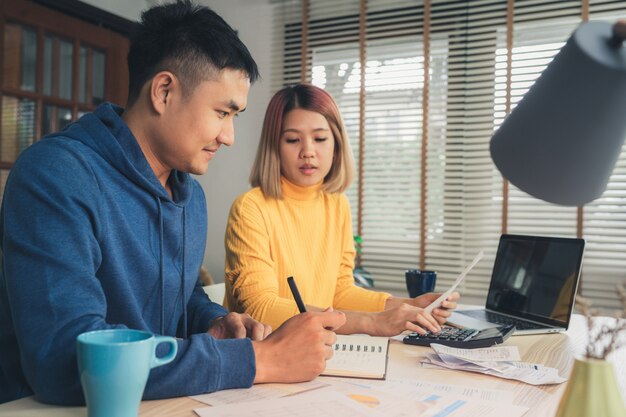 Young asian couple managing finances, reviewing their bank accounts using laptop computer