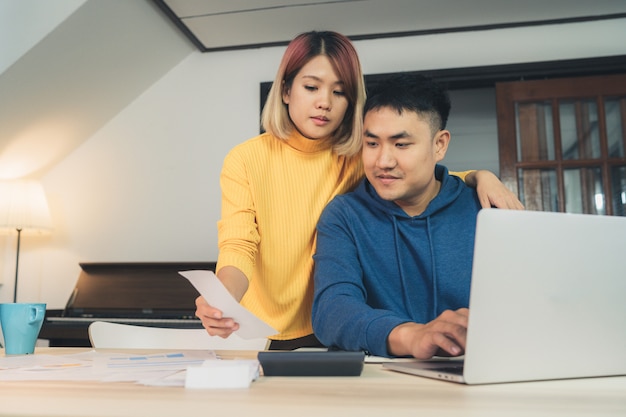 young asian couple managing finances, reviewing their bank accounts using laptop computer 