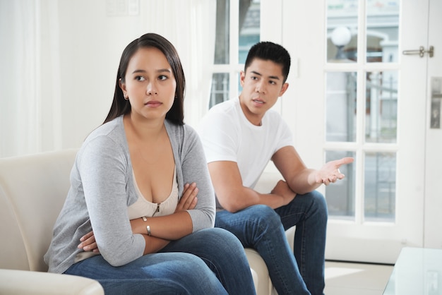 Young Asian couple sitting on couch at home and quarrelling