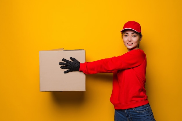 Молодая азиатская женщина доставки держит коробку изолированную на желтом