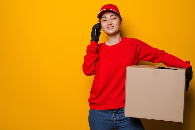 Young asian delivery woman holding box talking on the phone isolated