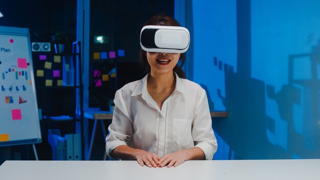 vr 안경 (가상 현실)을 사용하는 젊은 아시아 디자이너 여성이 현대 크리에이티브 홈 오피스의 밤에 소프트웨어 개발에서 모바일 앱을 테스트합니다. 코로나 바이러스 예방을위한 사회적 거리두기, 격리.