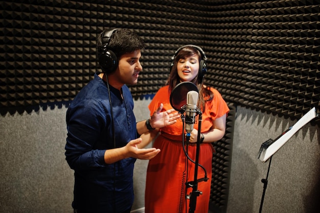 Young asian duet singers with microphone recording song in record music studio