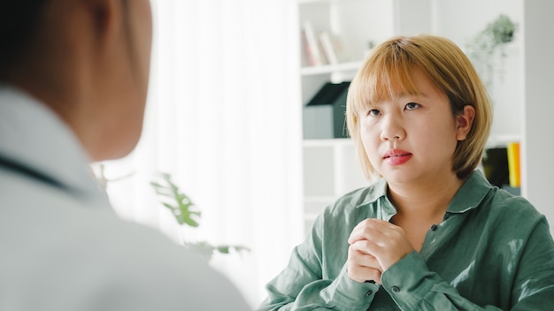 여자 환자와 결과 또는 증상을 논의하는 흰색 의료 제복을 입은 젊은 아시아 여성 의사