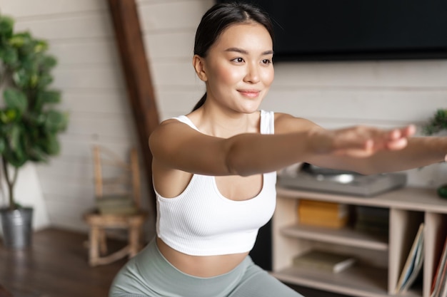 Молодая азиатская фитнес-женщина со здоровым подтянутым телом делает утреннюю тренировку приседаний в спортивной одежде ...