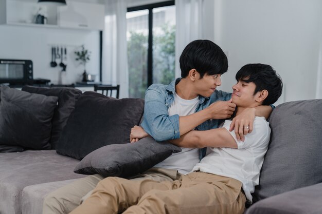 Young Asian Gay couple hug and kiss at home. Attractive Asian LGBTQ pride men happy relax spend romantic time together while lying sofa in living room .