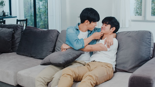 Young asian gay couple hug and kiss at home. attractive asian lgbtq+ pride men happy relax spend romantic time together while lying sofa in living room .