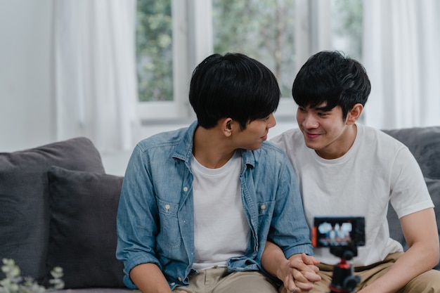 Young Asian gay couple influencer couple vlog at home. Teen korean LGBTQ men happy relax fun using camera record vlog video upload in social media while lying sofa in living room at house .