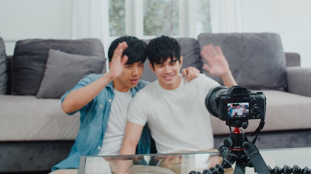 Free photo young asian gay couple influencer couple vlog at home. teen korean lgbtq+ men happy relax fun using camera record vlog video upload in social media while lying sofa in living room at house .