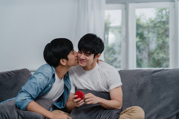 若いアジアの同性愛者のカップルが自宅で提案し、10代の韓国LGBTQ男性の幸せな笑顔はロマンチックな時間を提案し、結婚の驚きは家のリビングルームで結婚指輪を着用します。