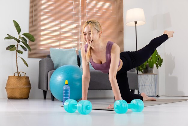 Young Asian girl in a sports uniform performs an exercise on a sports mat at home