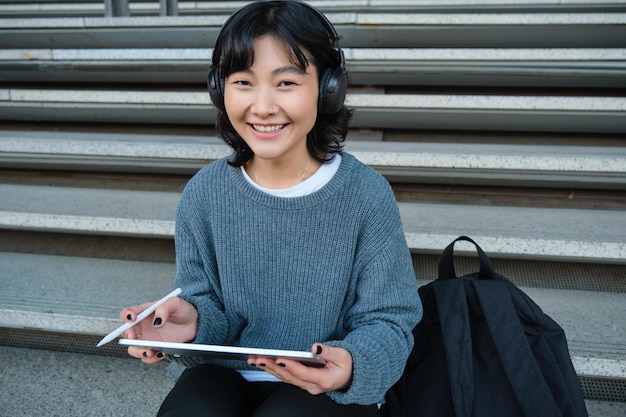 Free photo young asian girl student in headphones works on remote digital artist drawing on tablet with graphic