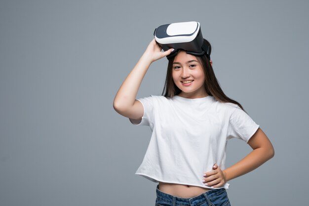 Молодая азиатская девушка смотря VR хотя и касание руки на воздухе на серой предпосылке