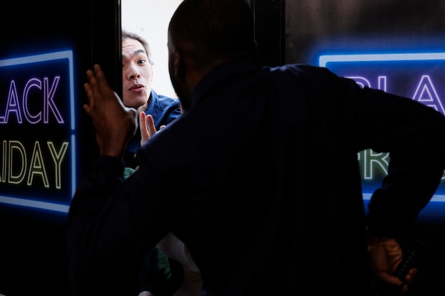 Foto gratuita giovane ragazzo asiatico che cerca di entrare nel negozio al dettaglio il black friday prima dell'orario di apertura, pazzo acquirente che litiga e discute con la guardia di sicurezza mentre si trova all'ingresso del centro commerciale