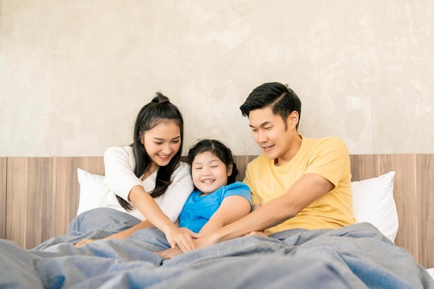 若いアジアの幸福家族のお父さんのお母さんと小さな娘は、自宅でベッドプレジャーで一緒に楽しい遊び手応援一緒に関係瞬間家族の概念