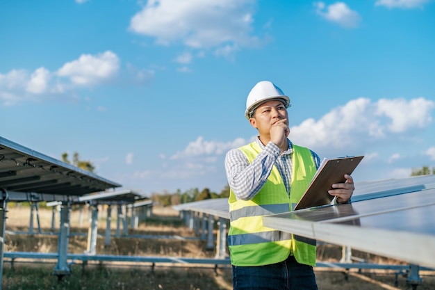 Young Asian Inspector Engineer man working at solar farm Technician or supervisor male in white helmet Checking operation of sun and photovoltaic solar panel in station copy space